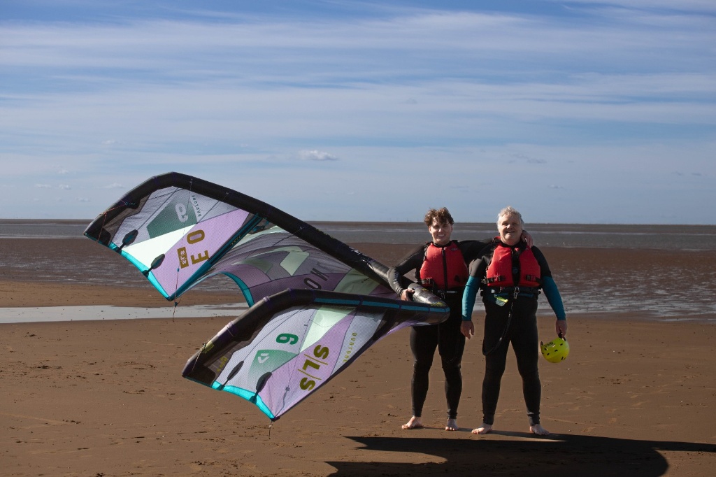 Nigel Marsh and instructor in red buoyancy aids holding large kite on Hunstanton Wash tidal flats North Norfolk UK under blue sky